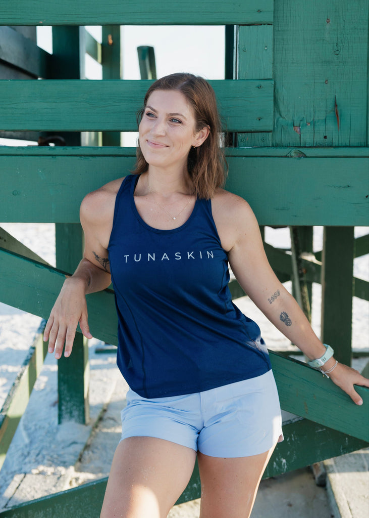 Woman wearing a navy tank top with 'TUNASKIN' branding, standing next to lifeguard stand