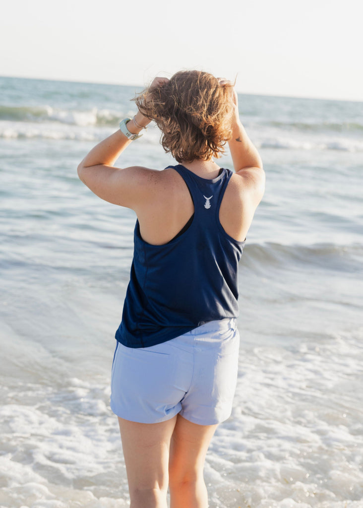 Person wearing a navy tank top and blue shorts standing on a beach.