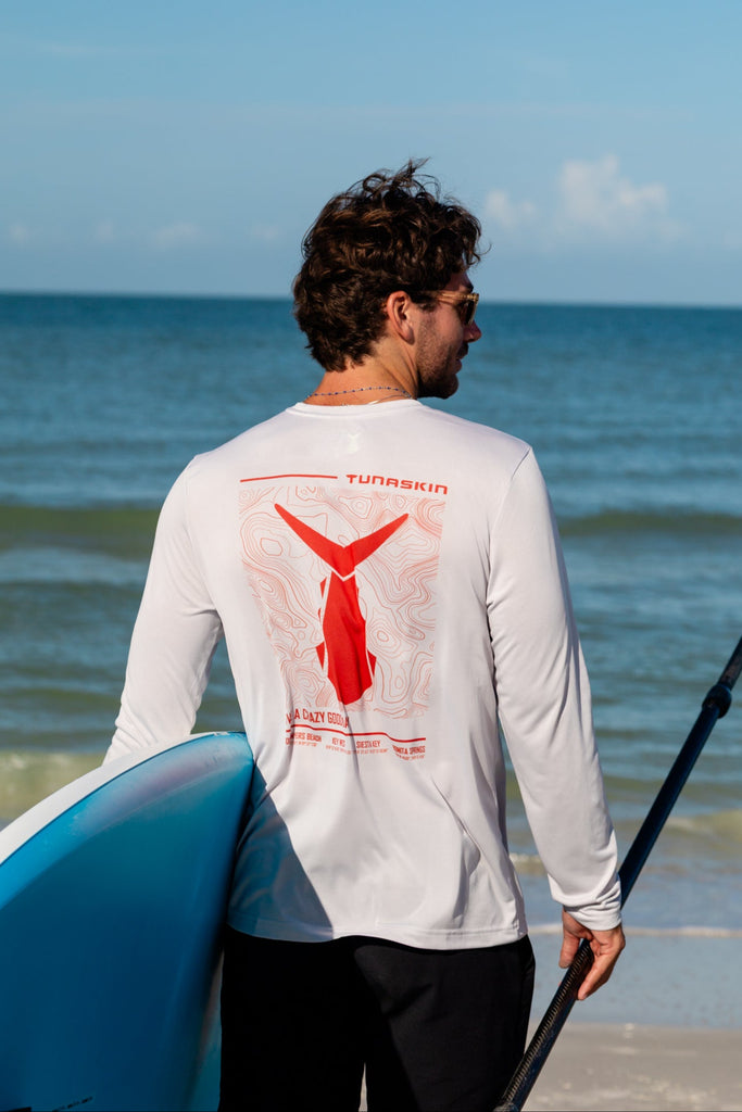 Man holding a paddle and a blue surfboard on a beach with ocean and sky in the background