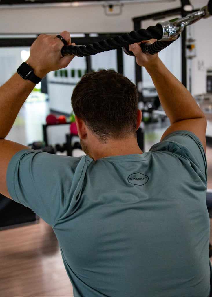 Person exercising with a pull-up bar in a gym setting with Tunaskin shirt