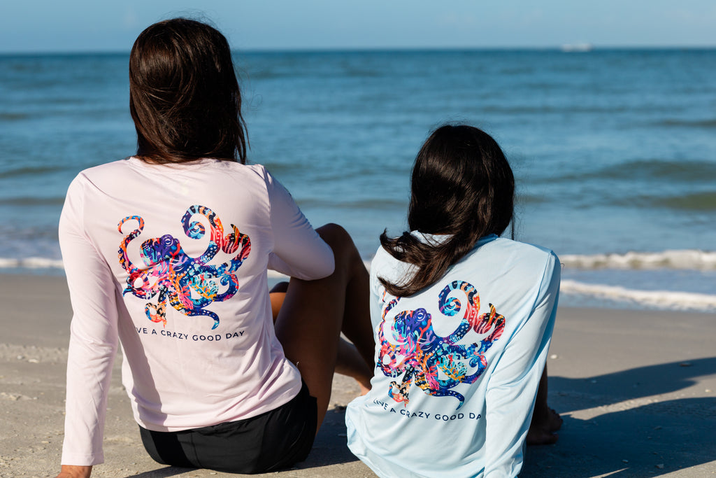 Two people sitting on a beach wearing shirts with colorful octopus designs.
