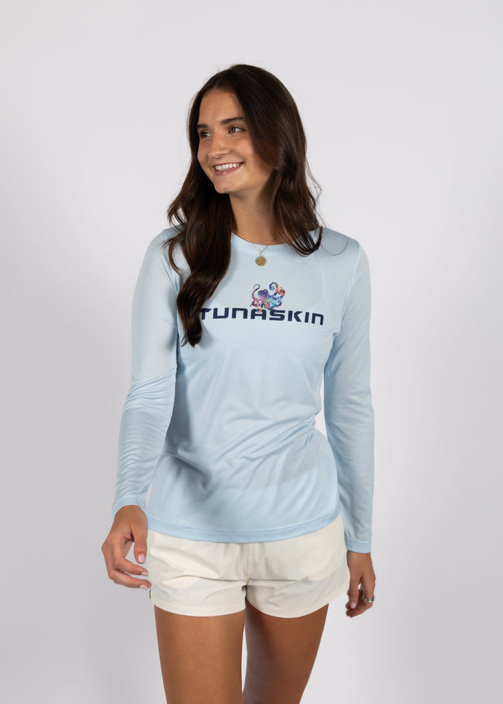 Woman wearing a light blue long-sleeve shirt with 'Tunaskin' logo on a white background