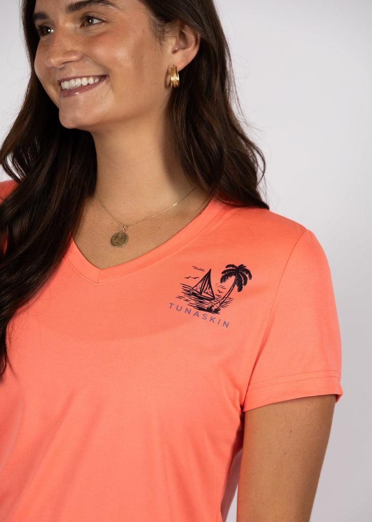 Woman wearing a coral t-shirt with a logo on a plain background