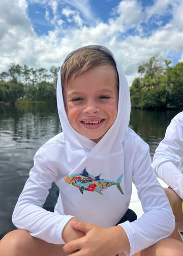 Child wearing a white Tunaskin hooded shirt with a colorful design outdoors