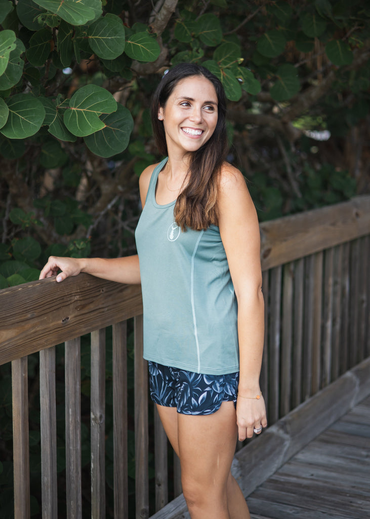 Woman in athletic wear standing on a wooden deck with green foliage in the background